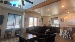 A spacious living area with a ceiling fan, a dining table, and a kitchen area with bar stools. - Beautiful Bear Lake House, with big grassy yard, 4 mins to North Beach. (St Charles)