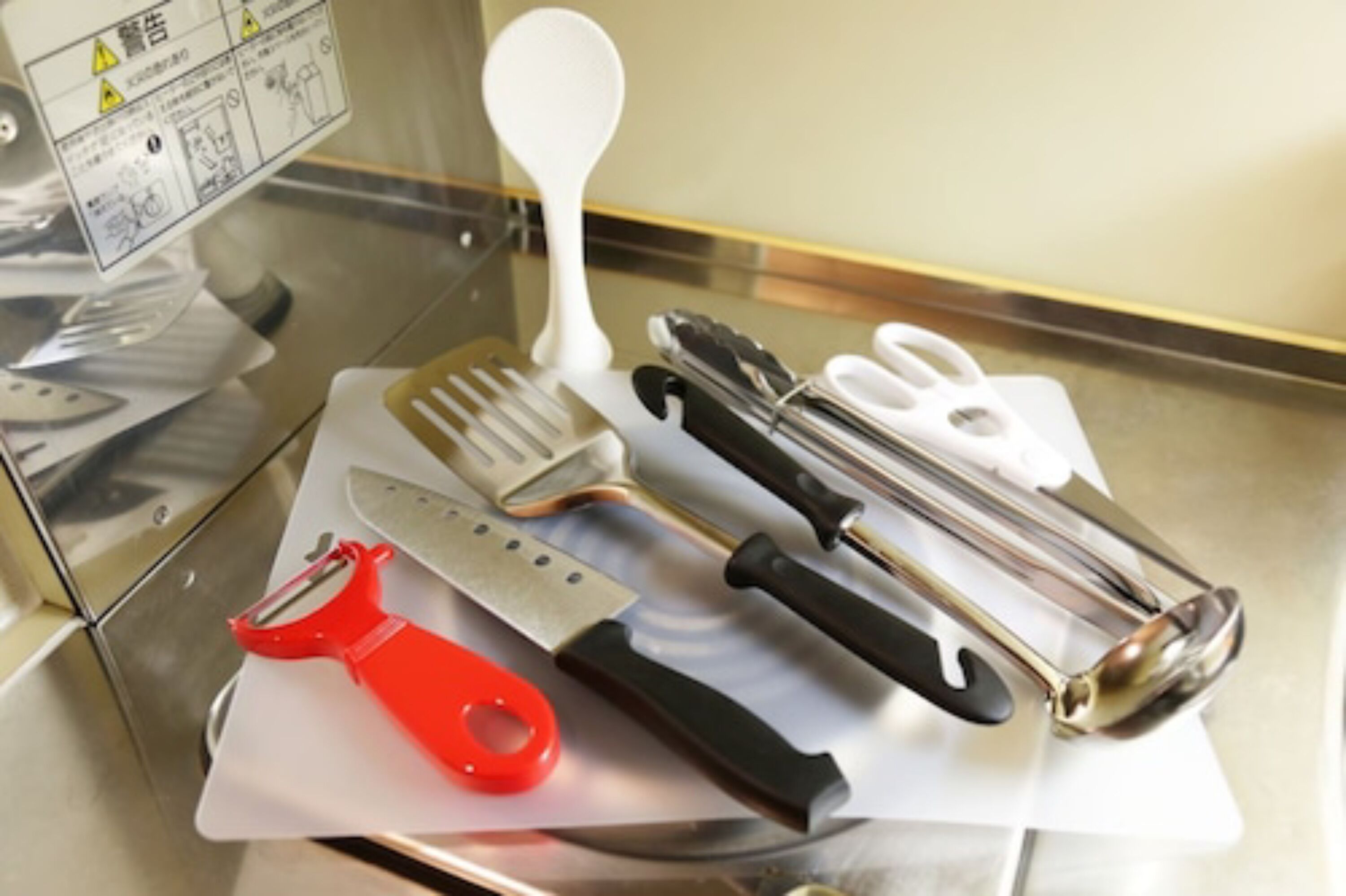 A stainless steel table with various kitchen utensils including a red peeler, a knife, a fork, and a white brush.