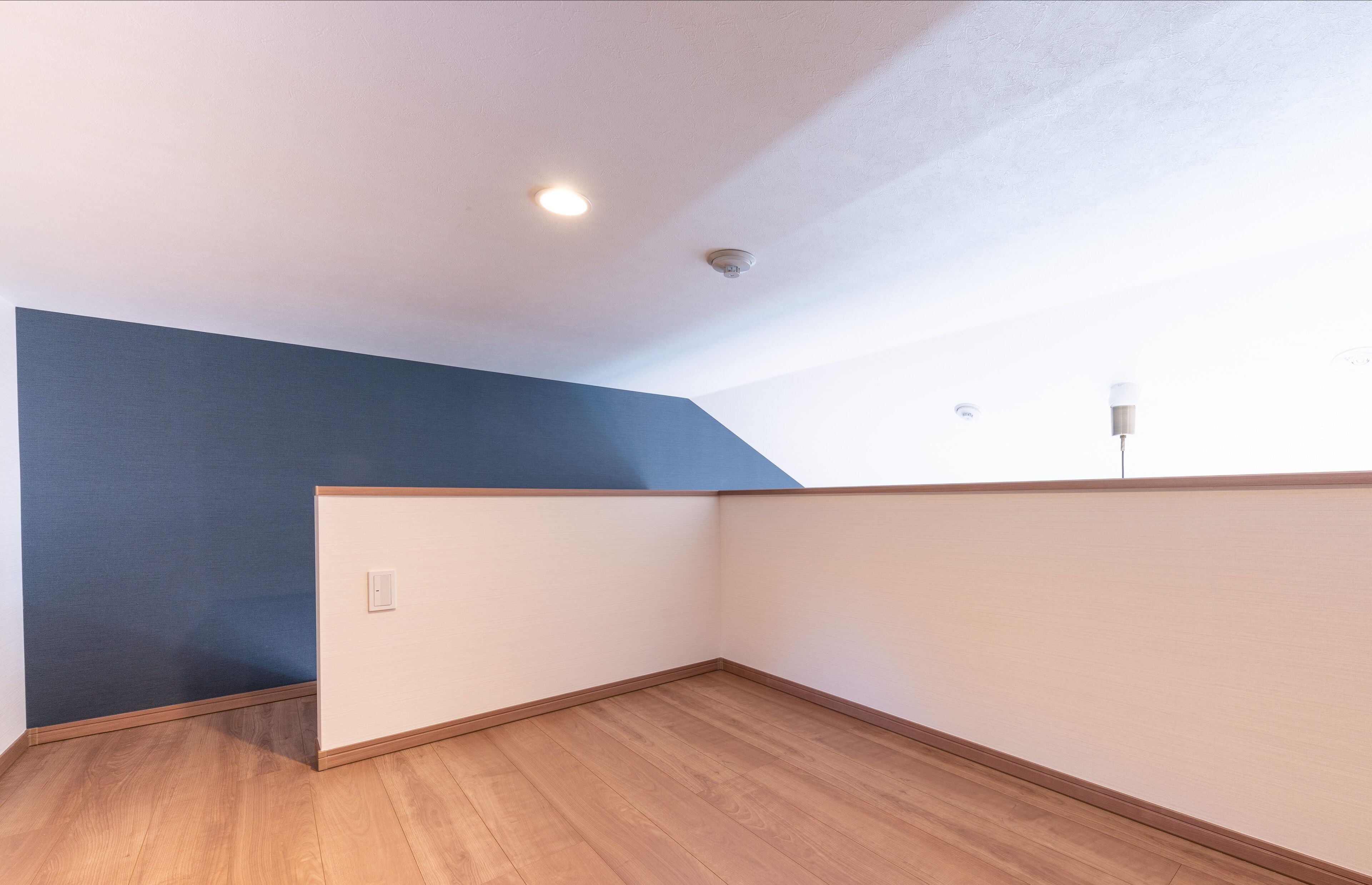 A corner room with a sloped ceiling, wooden flooring, and a blue accent wall.