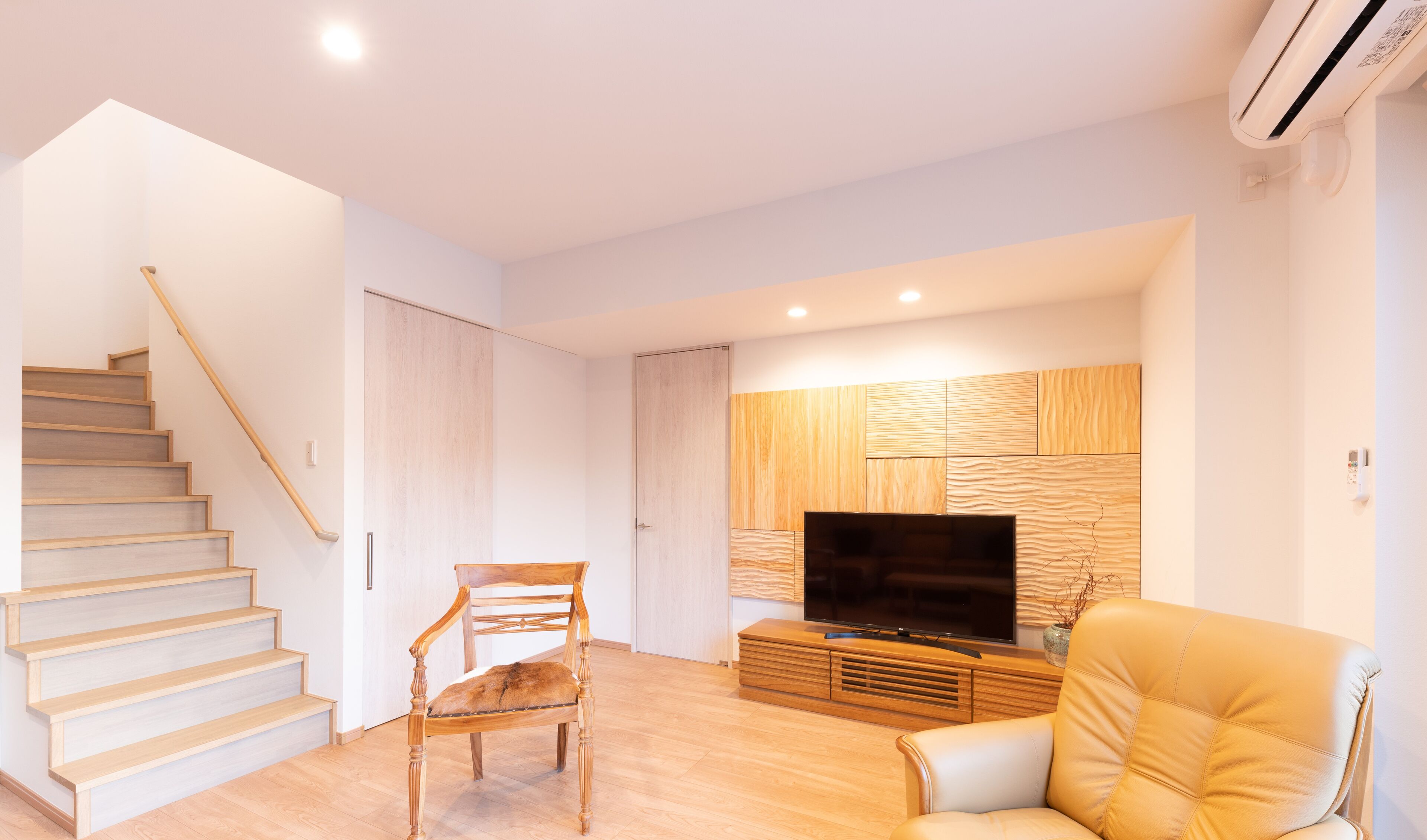 A modern living room with a wooden staircase, a flat-screen TV, a leather sofa, and a wooden entertainment unit.