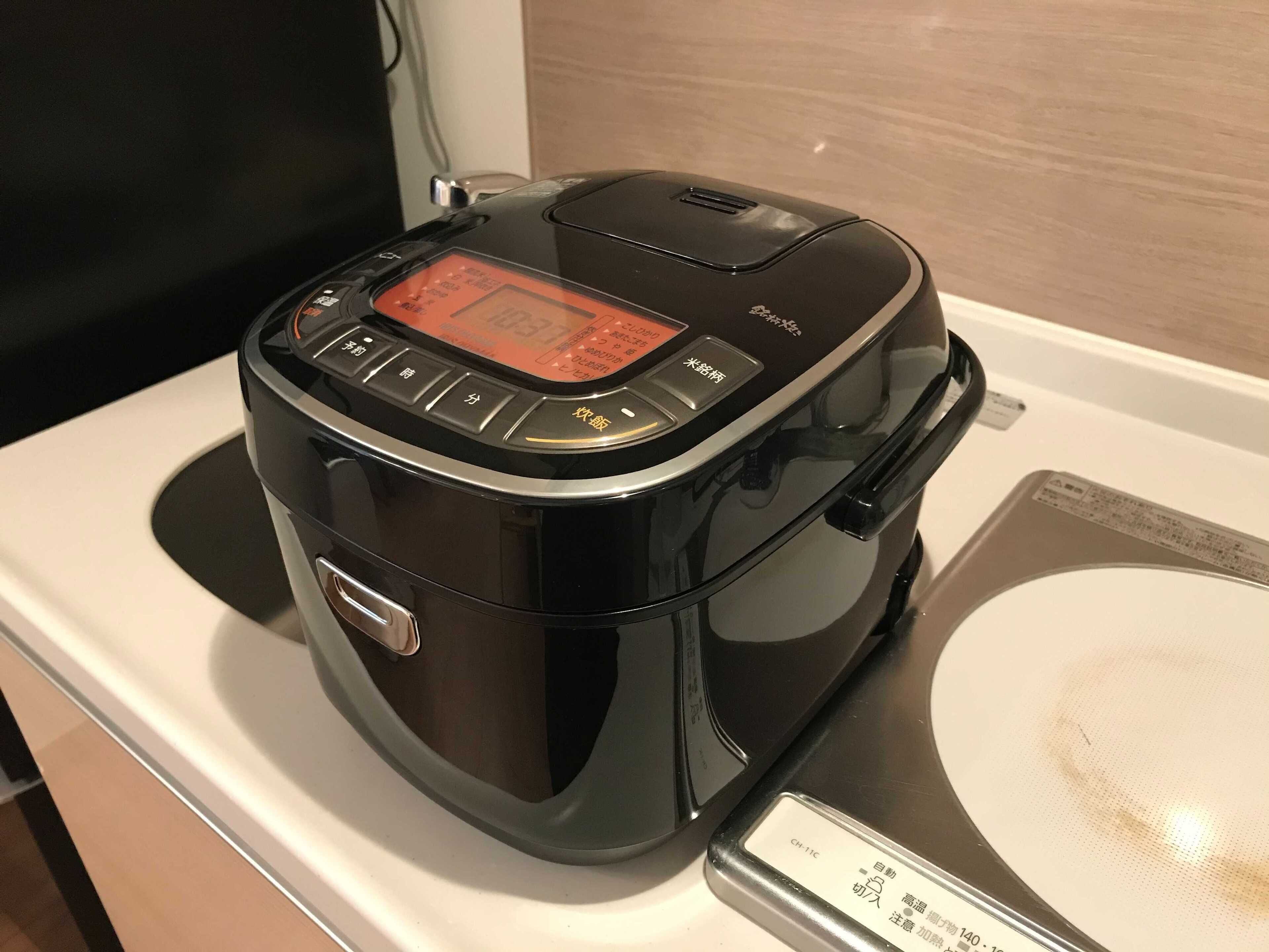 Una cocedora de arroz negra con pantalla digital y botones sobre una encimera blanca.