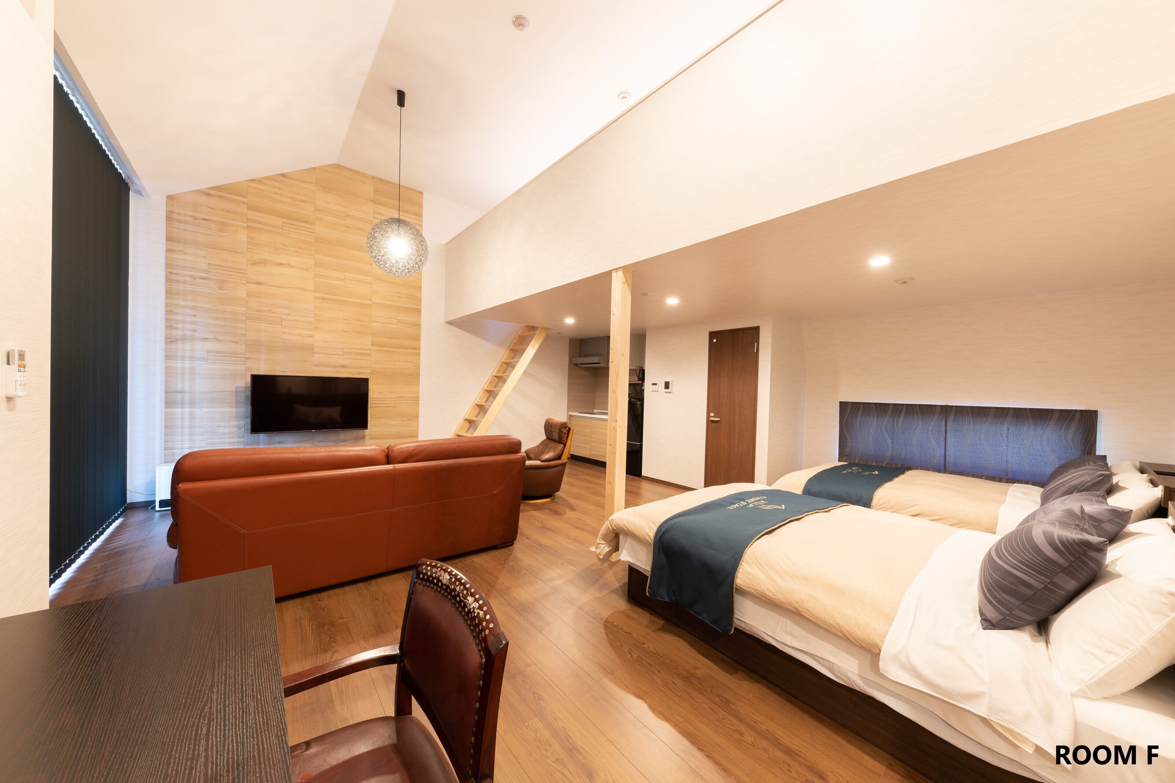 A modern hotel room with a wooden floor, a sofa, a bed with a headboard, a TV, and a staircase leading to another room.