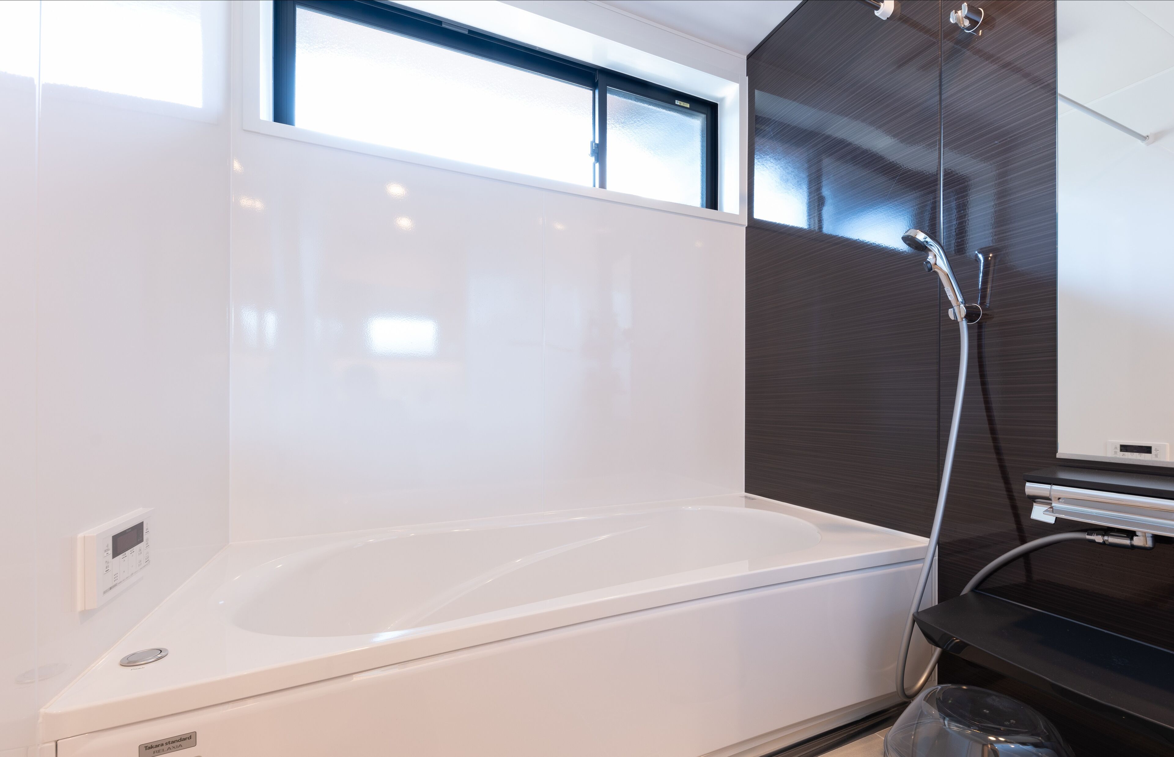 A modern bathroom with a white bathtub, a glass shower enclosure, and a control panel on the wall.