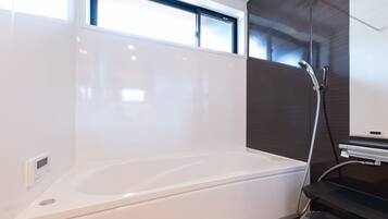 A modern bathroom with a white bathtub, a glass shower enclosure, and a control panel on the wall.