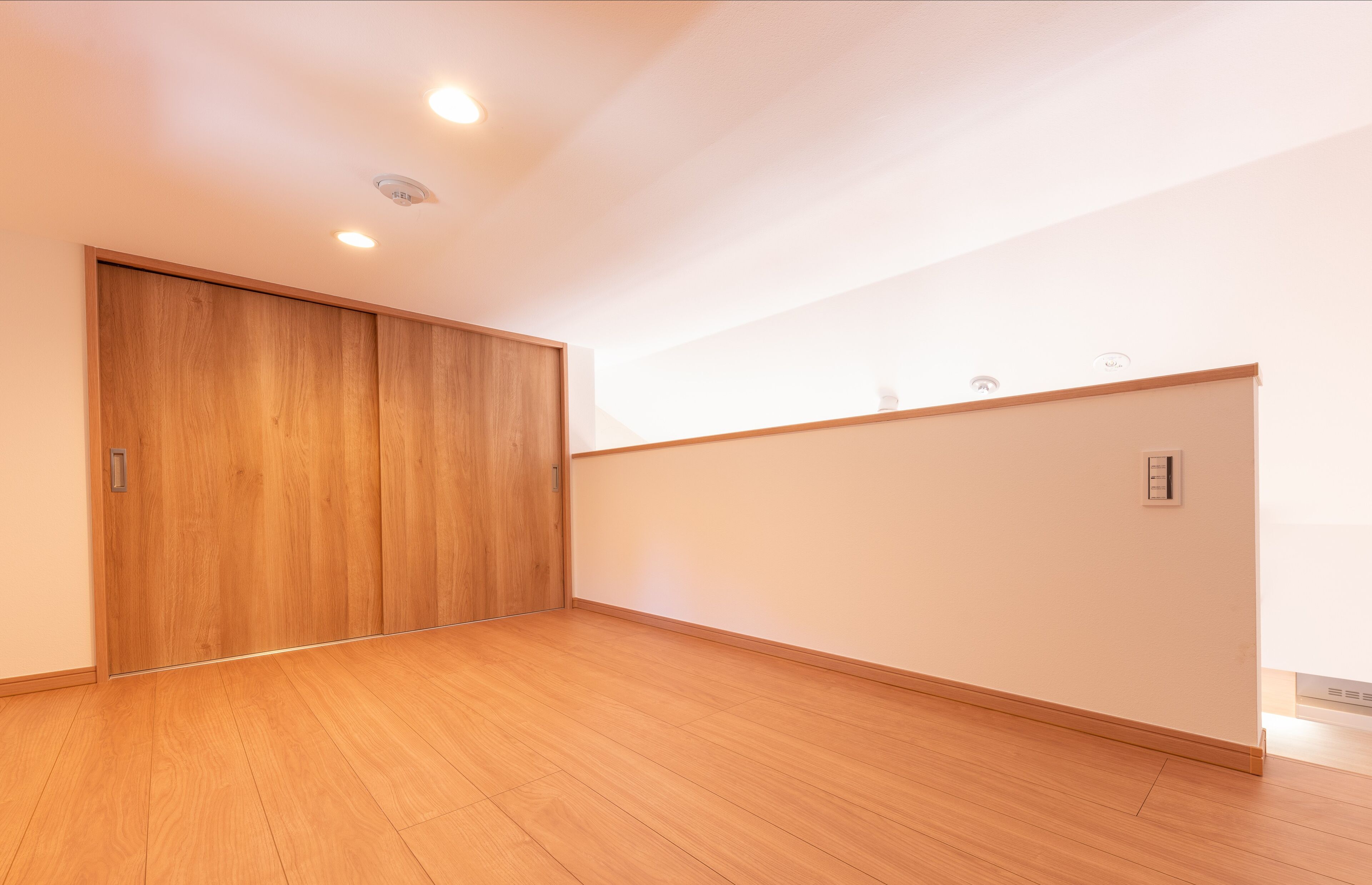 Una habitación amplia con suelo de madera, un gran ventanal corredera y una pared blanca con termostato.