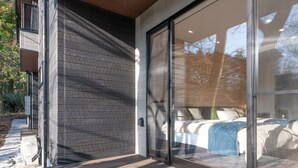 Un dormitorio moderno con un gran ventanal corredero, una cama con ropa de cama blanca y vistas al exterior.