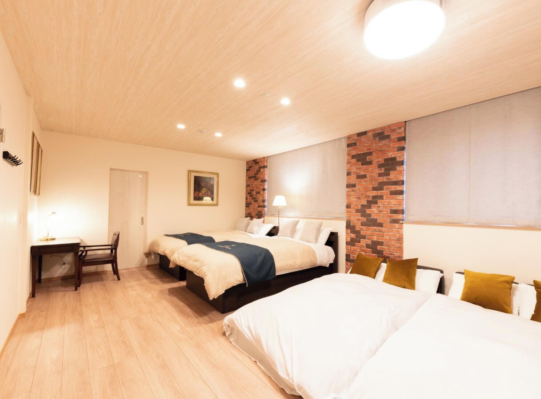 Ein Hotelzimmer mit Holzboden, zwei Betten, einem Schreibtisch und einer Wand mit Backsteinverkleidung.