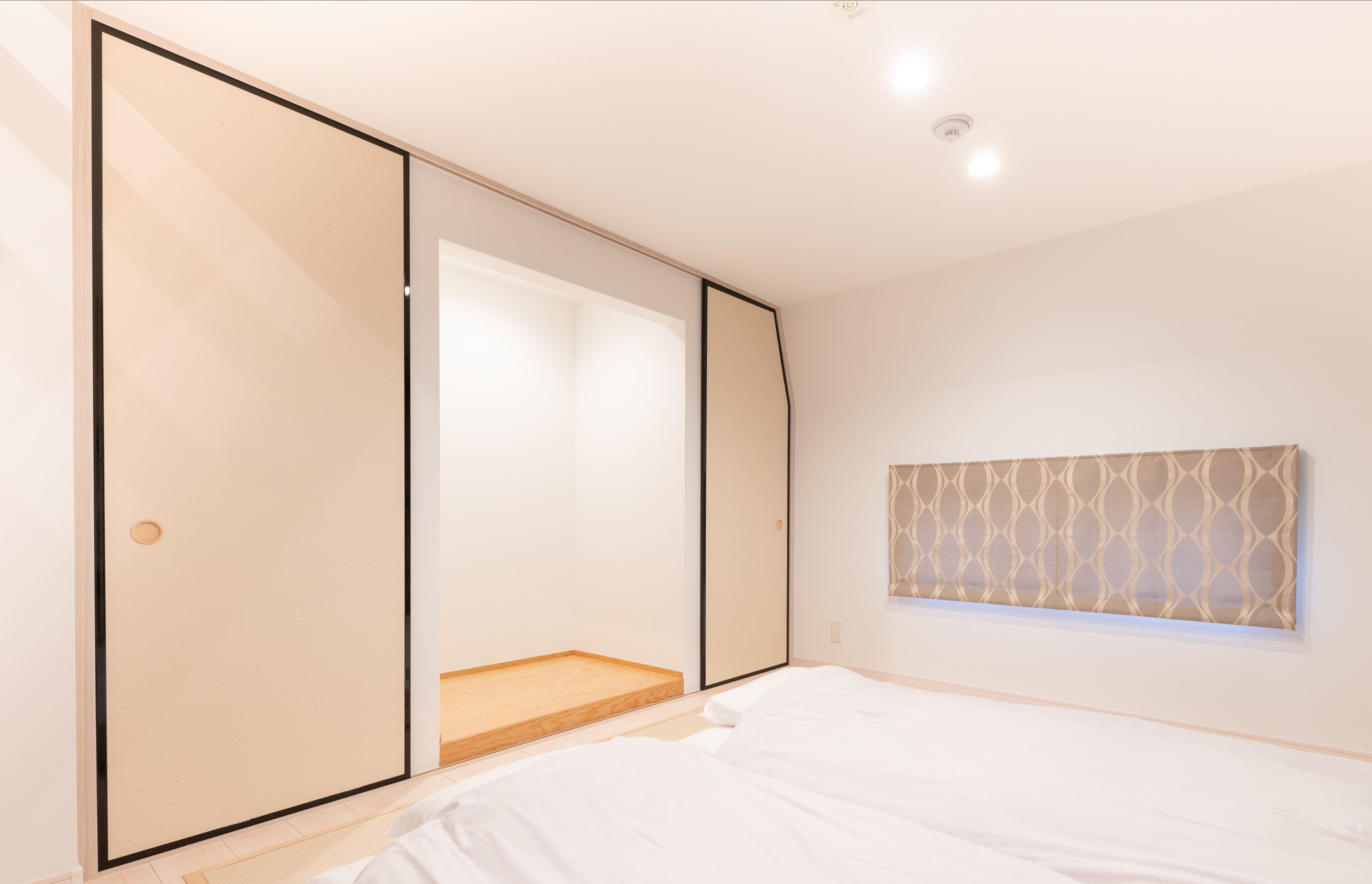 Ein Schlafzimmer mit einer großen Schiebetür, einem Bett, einer kleinen Holzplattform und einer Wanddekoration mit Muster.