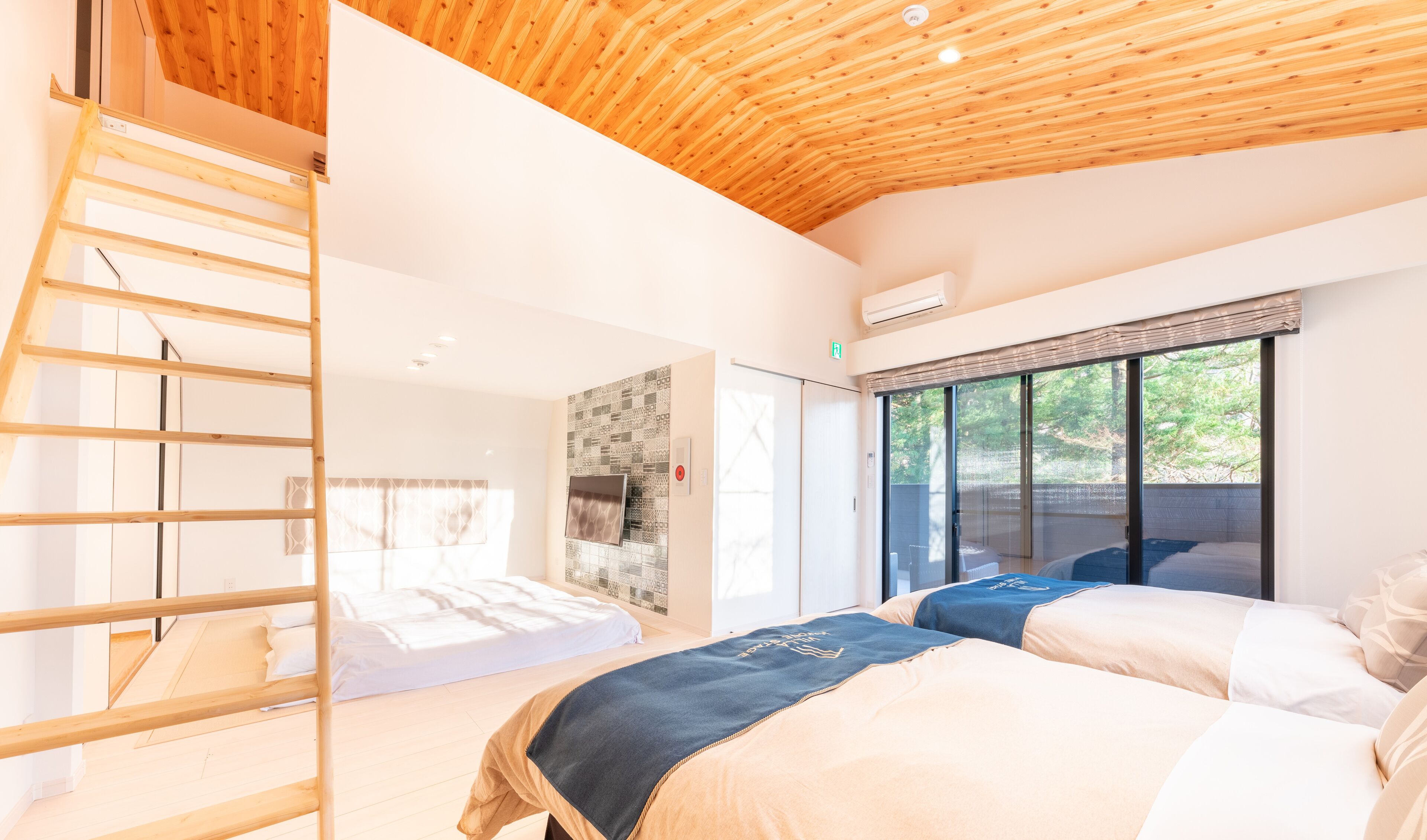 A modern bedroom with a wooden ceiling, a built-in bed, a ladder, and a large window with a view of greenery.
