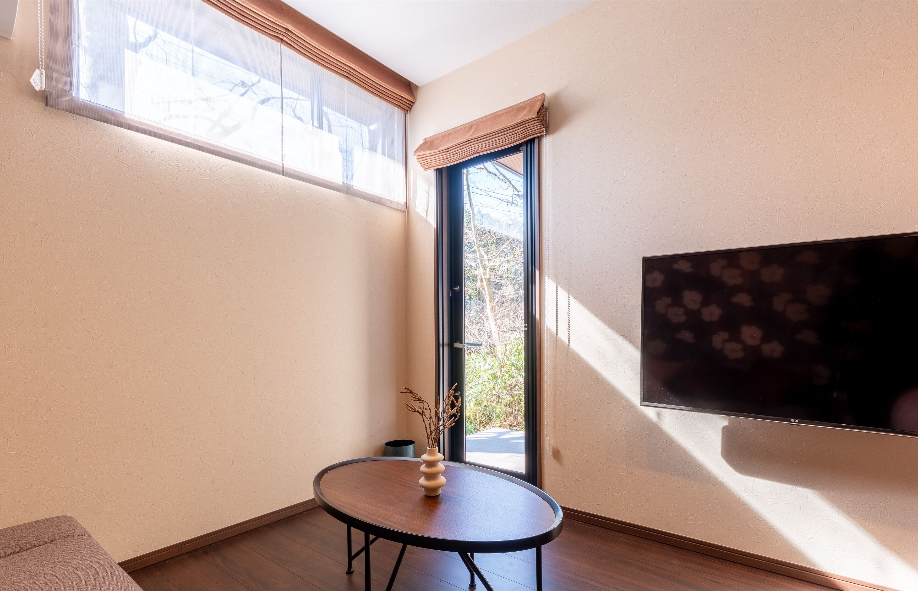 Una habitación con un ventanal grande, un televisor de pantalla plana y una pequeña mesa redonda con un jarrón.