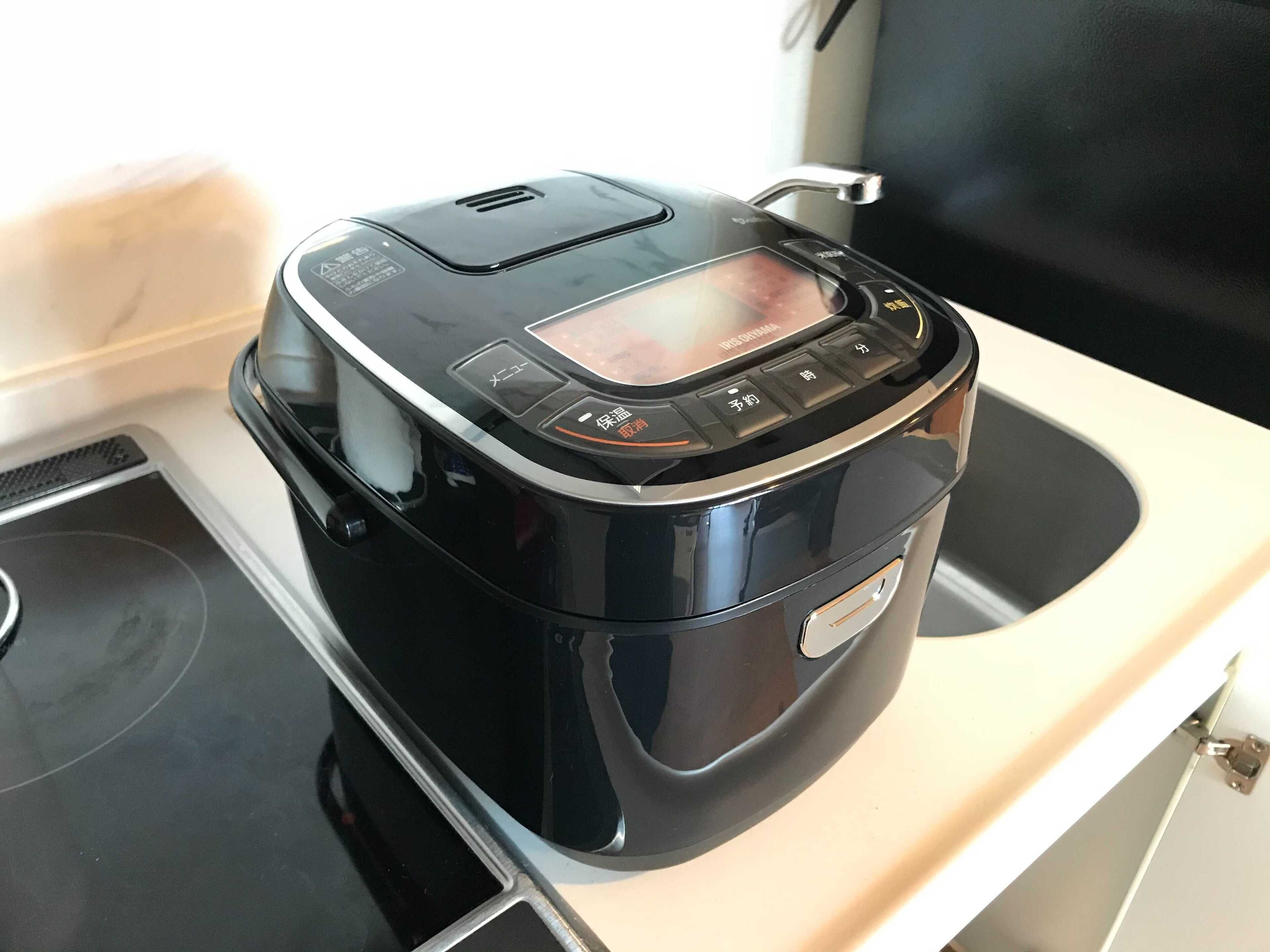 A black electric rice cooker on a kitchen counter.