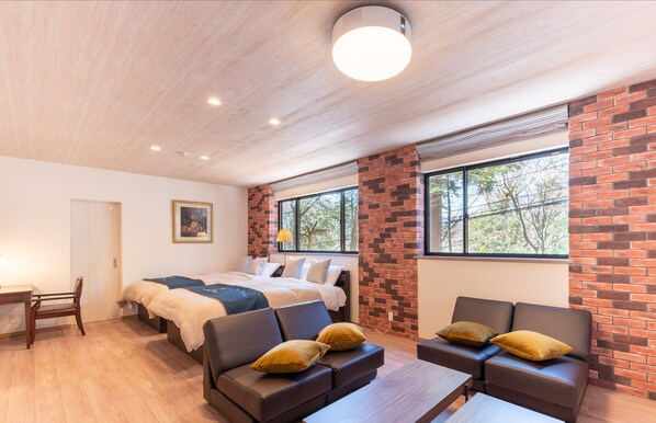 A modern room with a bed, two sofas, a desk, and large windows.