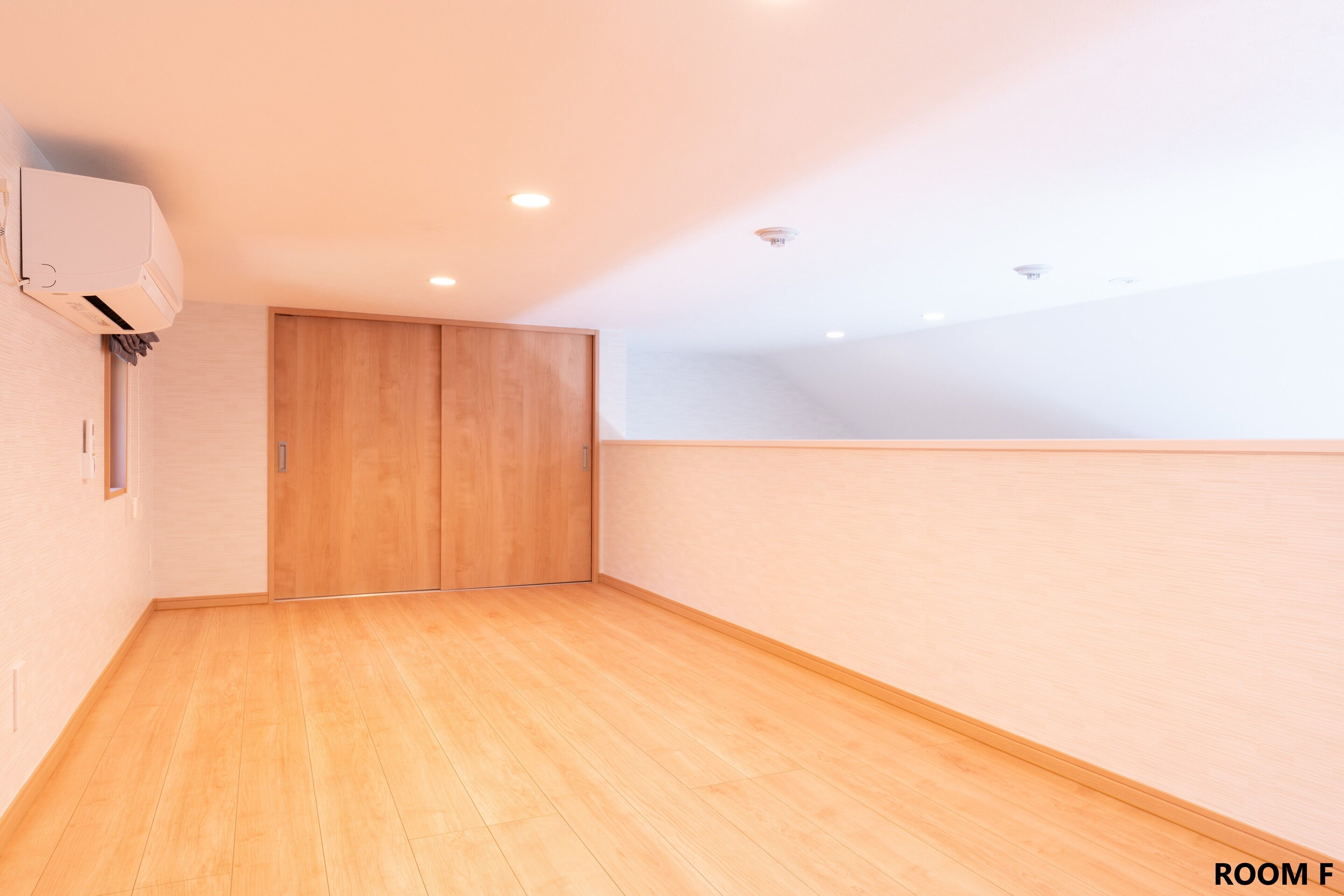 A room with wooden flooring, a ceiling-mounted air conditioner, and a wooden door.