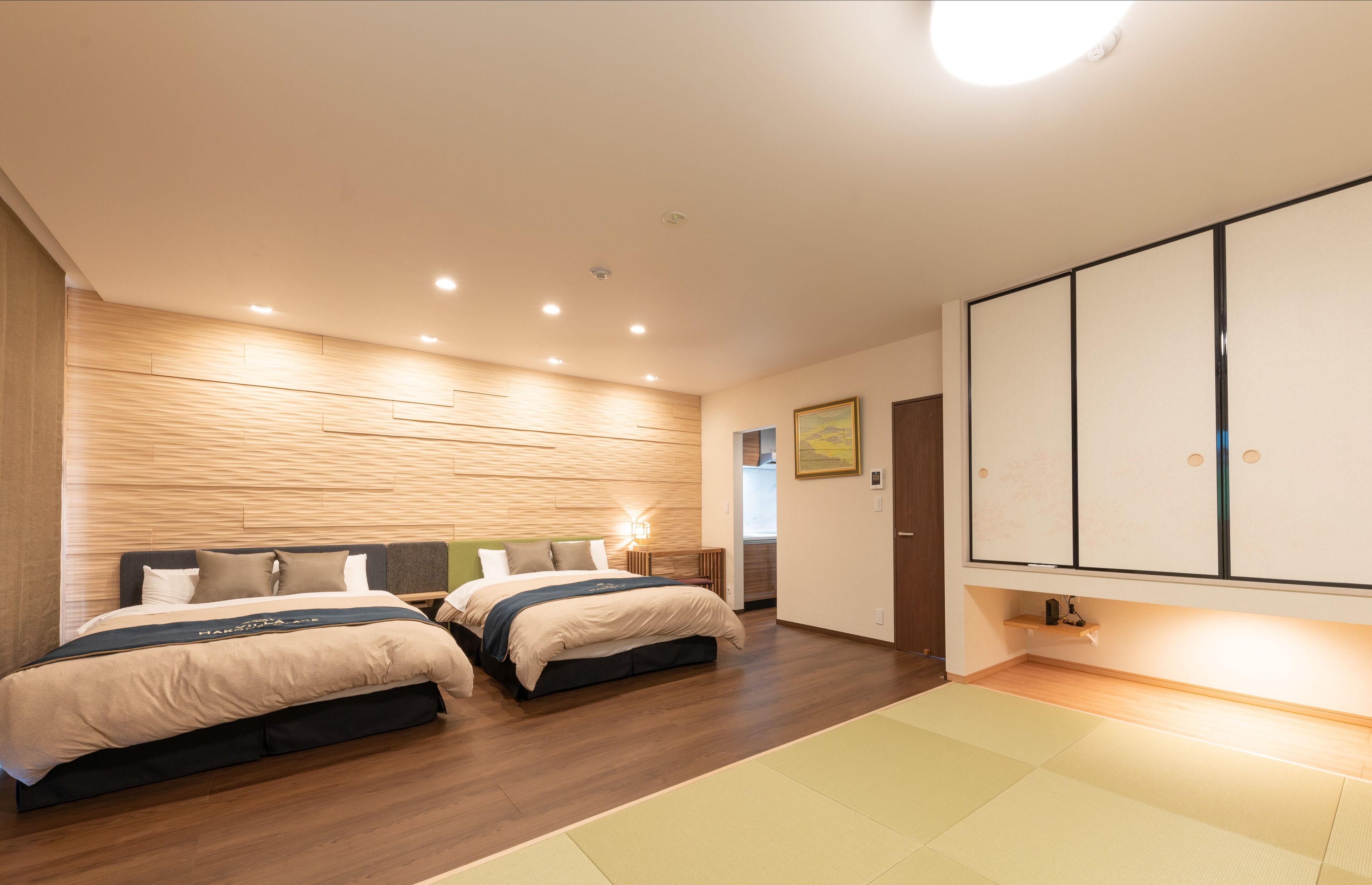 A modern hotel room with two beds, a wooden wall panel, a large cabinet, and a tatami mat floor.