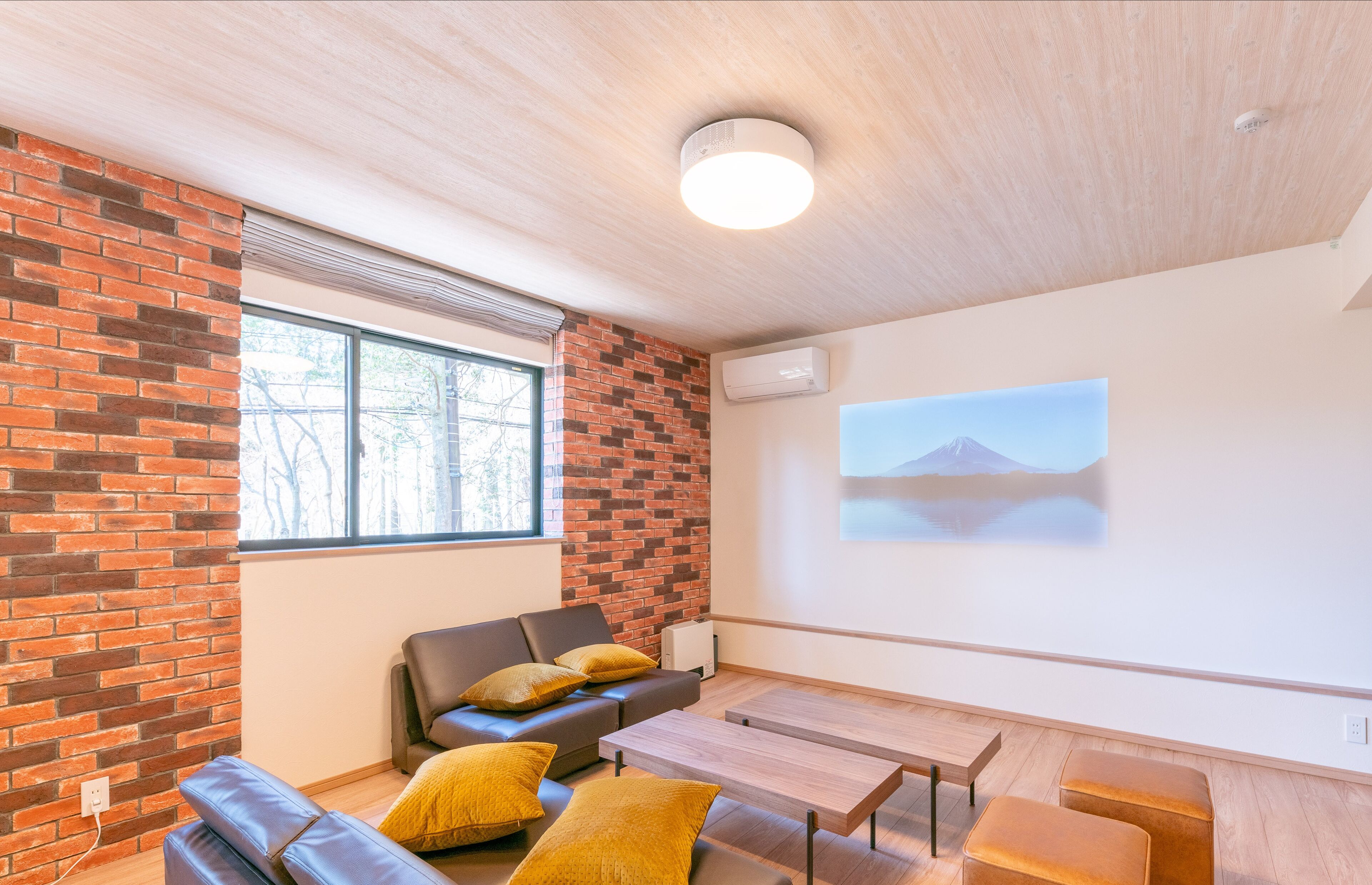 Une pièce moderne avec un mur en briques, un canapé en cuir, une table en bois et un écran de projection affichant une image de montagne.