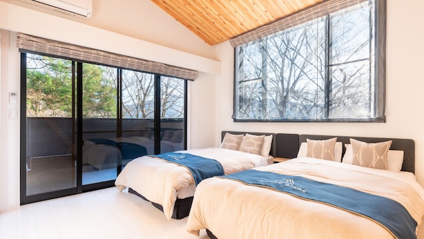 Un dormitorio con dos camas, ventanas amplias y techo de madera.