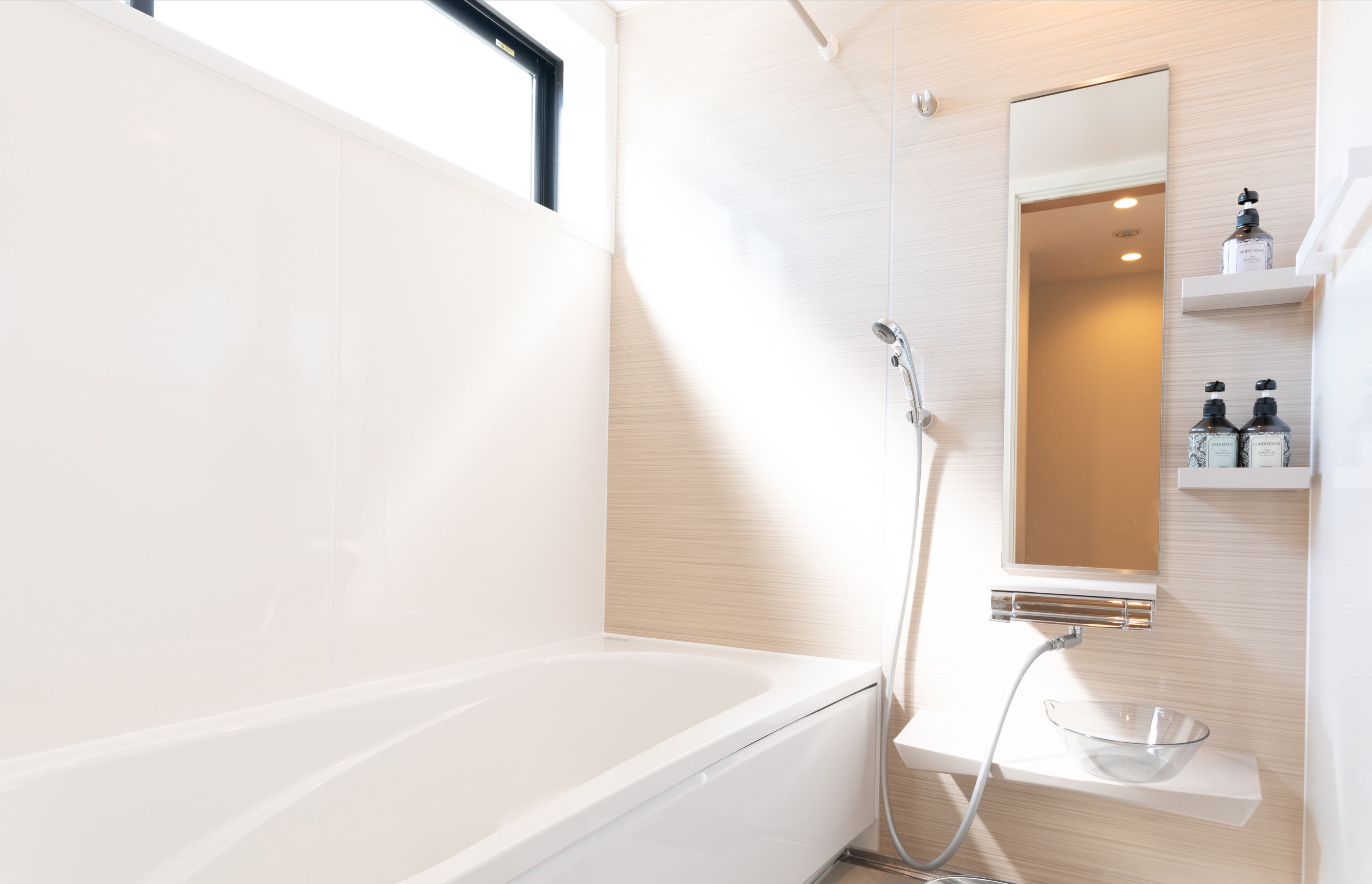 A modern bathroom with a bathtub, a shower, a mirror, and a shelf with toiletries.