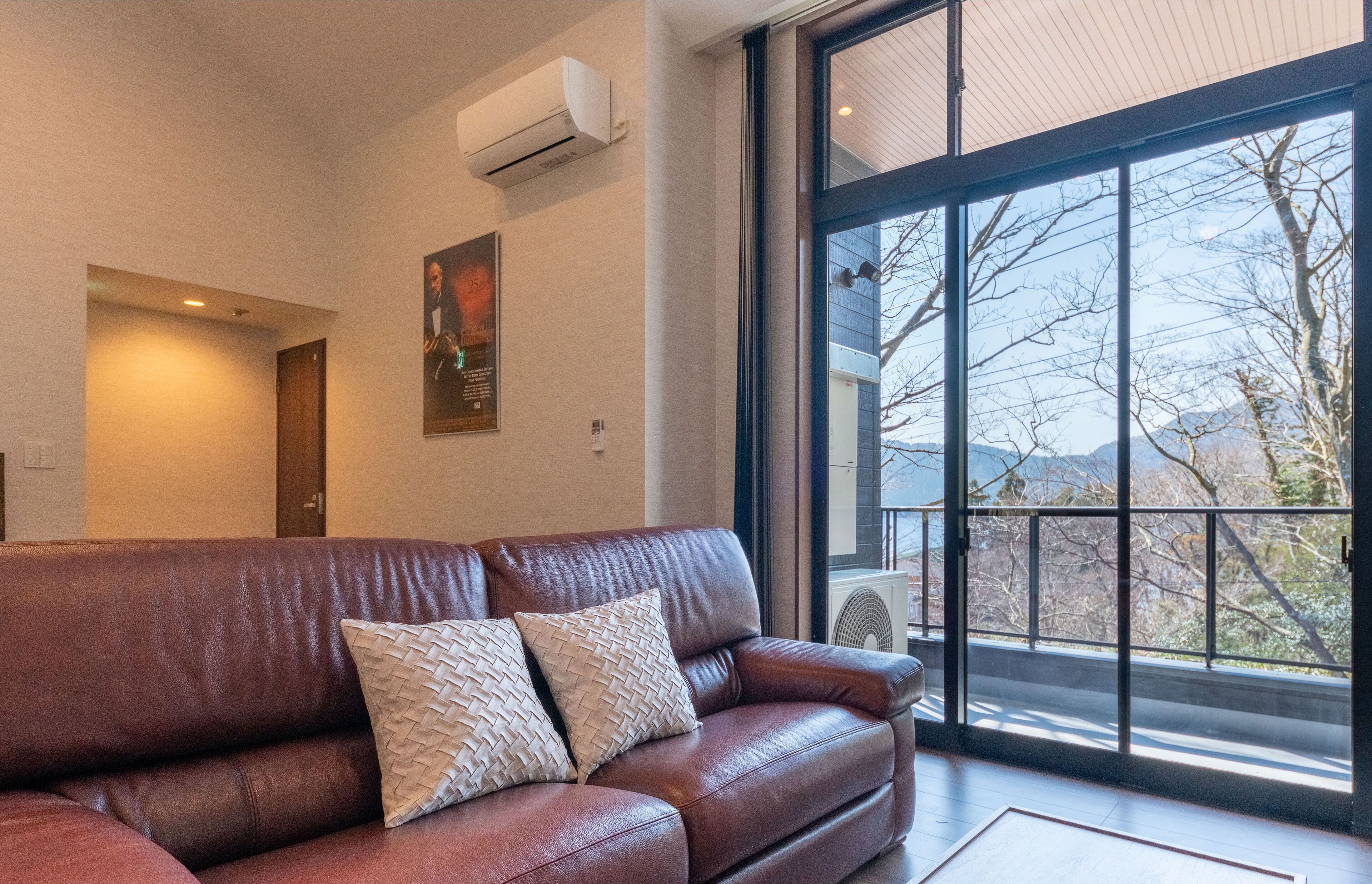 A modern living room with a leather sofa, large windows, and a view of mountains.