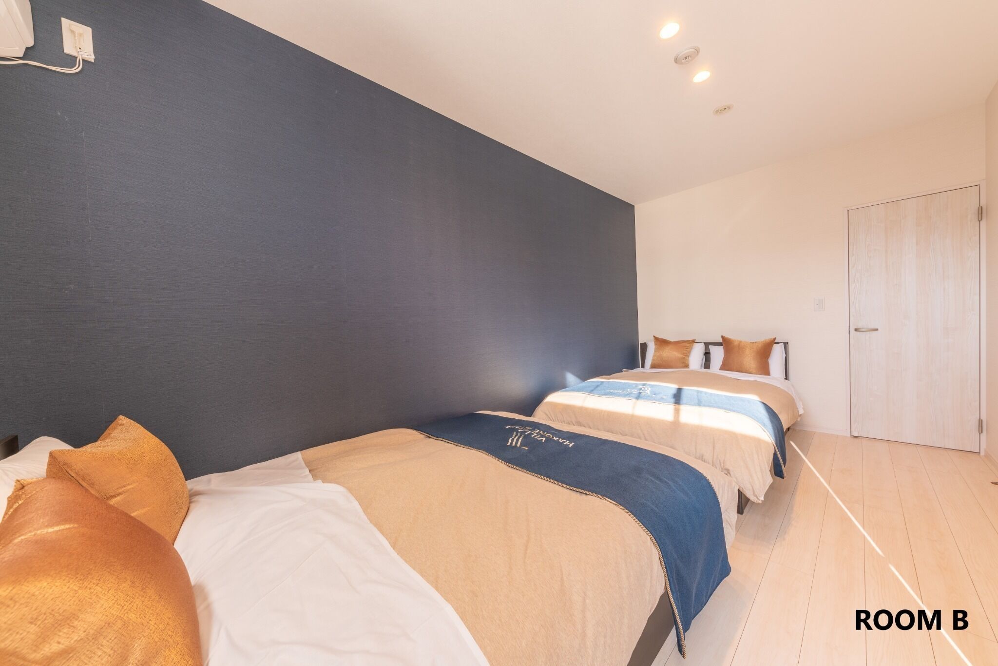 Ein Hotelzimmer mit zwei Betten, einer dunklen Wand, einem hellen Boden und einer Tür.