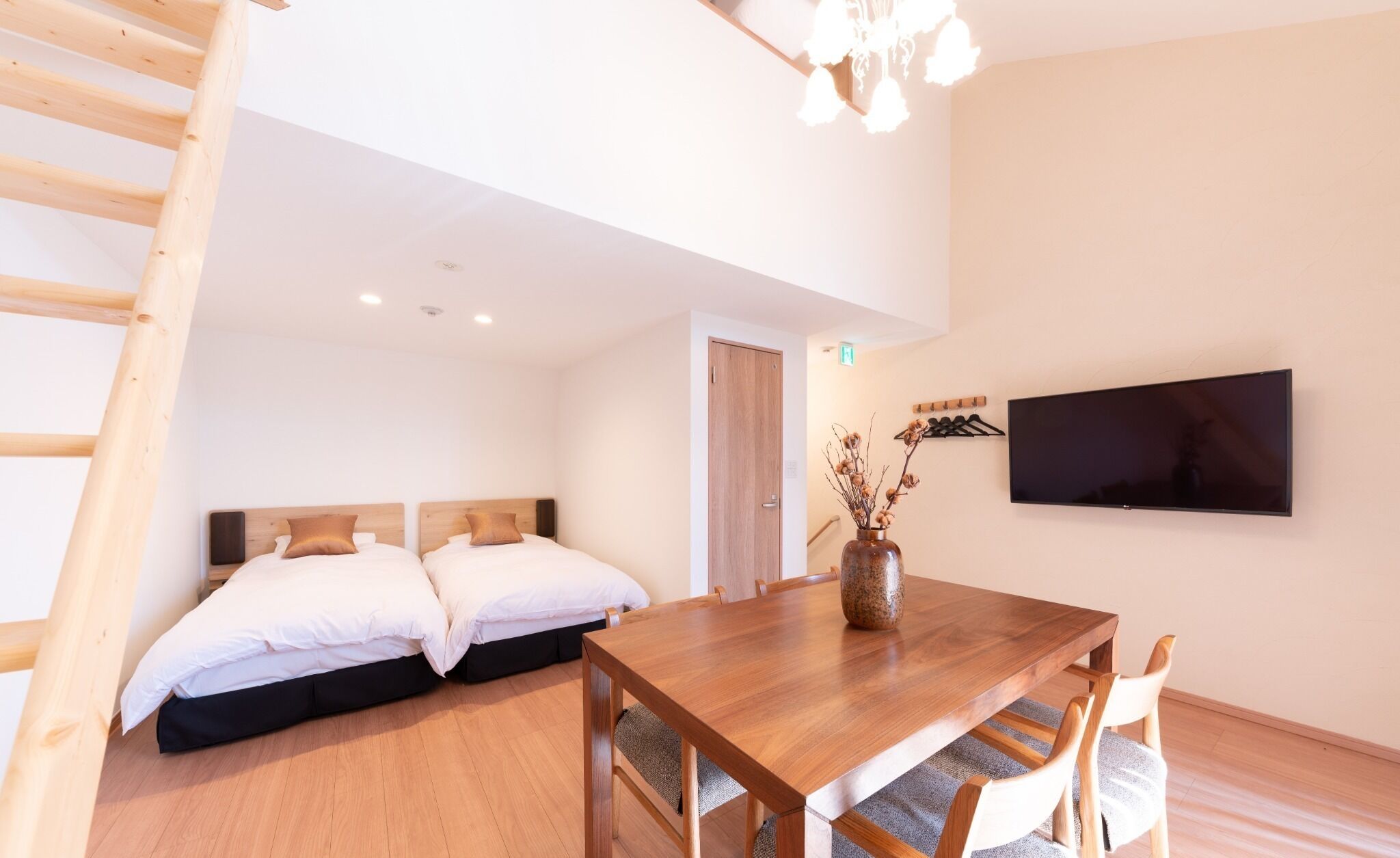 Ein Schlafzimmer mit zwei Betten, einem Holztisch und einem an der Wand befestigten Fernseher.