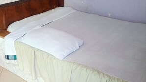 A bed with a white mattress, a beige bed skirt, and a wooden headboard. - Smartie Guest House (Nakuru)