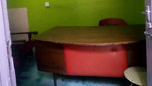 A room with a green wall, a wooden table with a red cushion, a chair, and a small shelf with a picture frame. - Smartie Guest House (Nakuru)