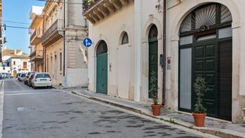 Una stretta via fiancheggiata da auto parcheggiate e palazzi con finestre e porte ad arco.