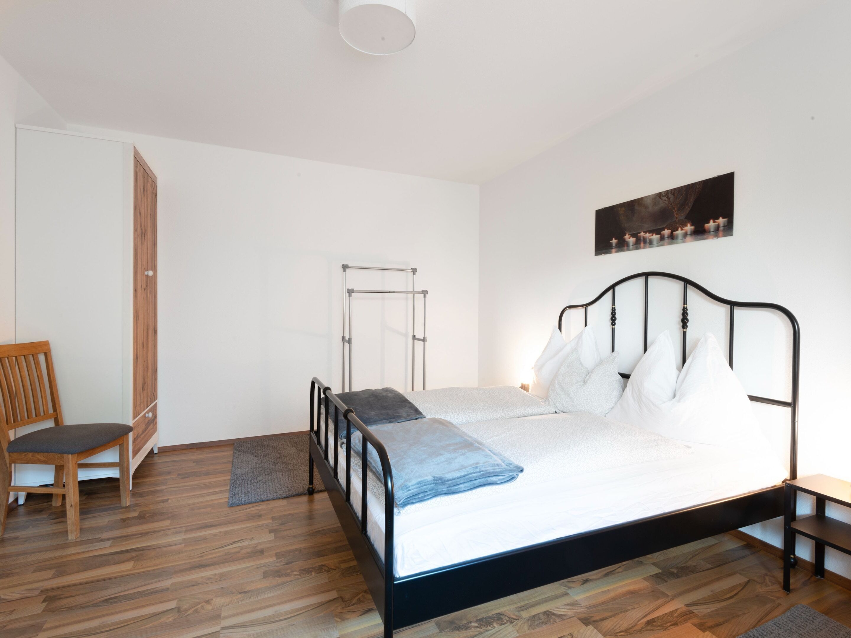 Une chambre à coucher avec un lit en métal, une chaise en bois, une armoire en bois et un tableau accroché au mur.