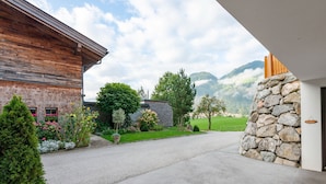 A modern building with a stone facade, a wooden deck, and a well-maintained garden with various plants and flowers.