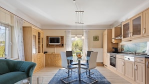 Een moderne keuken met houten keukenkastjes, een eettafel met stoelen, een glazen salontafel en een blauw vloerkleed.