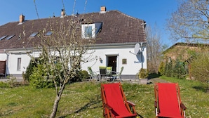 Een huis met een schuin dak, een schotelantenne en twee rode loungestoelen in de tuin.