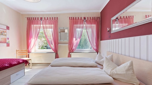 Een slaapkamer met een bed, een stoel, een raam met gordijnen, een radiator en een spiegel aan de muur.