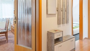 Une pièce avec une porte en bois, un miroir, une petite armoire et un lit à l’arrière-plan.
