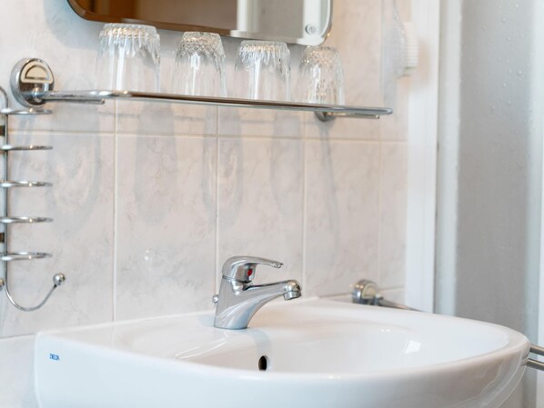 Une salle de bain avec un lavabo blanc, un robinet chromé et une étagère en verre au-dessus du lavabo.