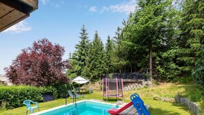 Un jardin avec une piscine, un toboggan et un trampoline.