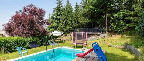 Un patio trasero con piscina, tobogán y trampolín.