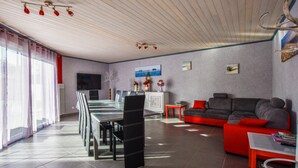 A modern living room with a dining area, a grey sofa with red cushions, a TV, and a fireplace. - Poolside Escape by Arcachon (La Teste-de-Buch)