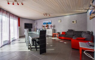 Una sala de estar moderna con comedor, un sofá gris con cojines rojos, un televisor y una chimenea.