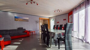 A modern living room with a sofa, dining table, chairs, and a view through an arched doorway. - Poolside Escape by Arcachon (La Teste-de-Buch)