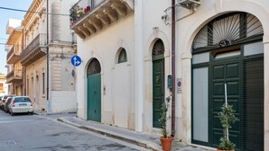 A street with parked cars, a building with green doors, and a no parking sign.