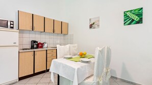 A small, clean kitchen with wooden cabinets, a microwave, and a coffee maker. There is a dining table with a white tablecloth and a chair with a white cover. - Apartment in Jasenice Near Maslenica Beach (Jasenice)