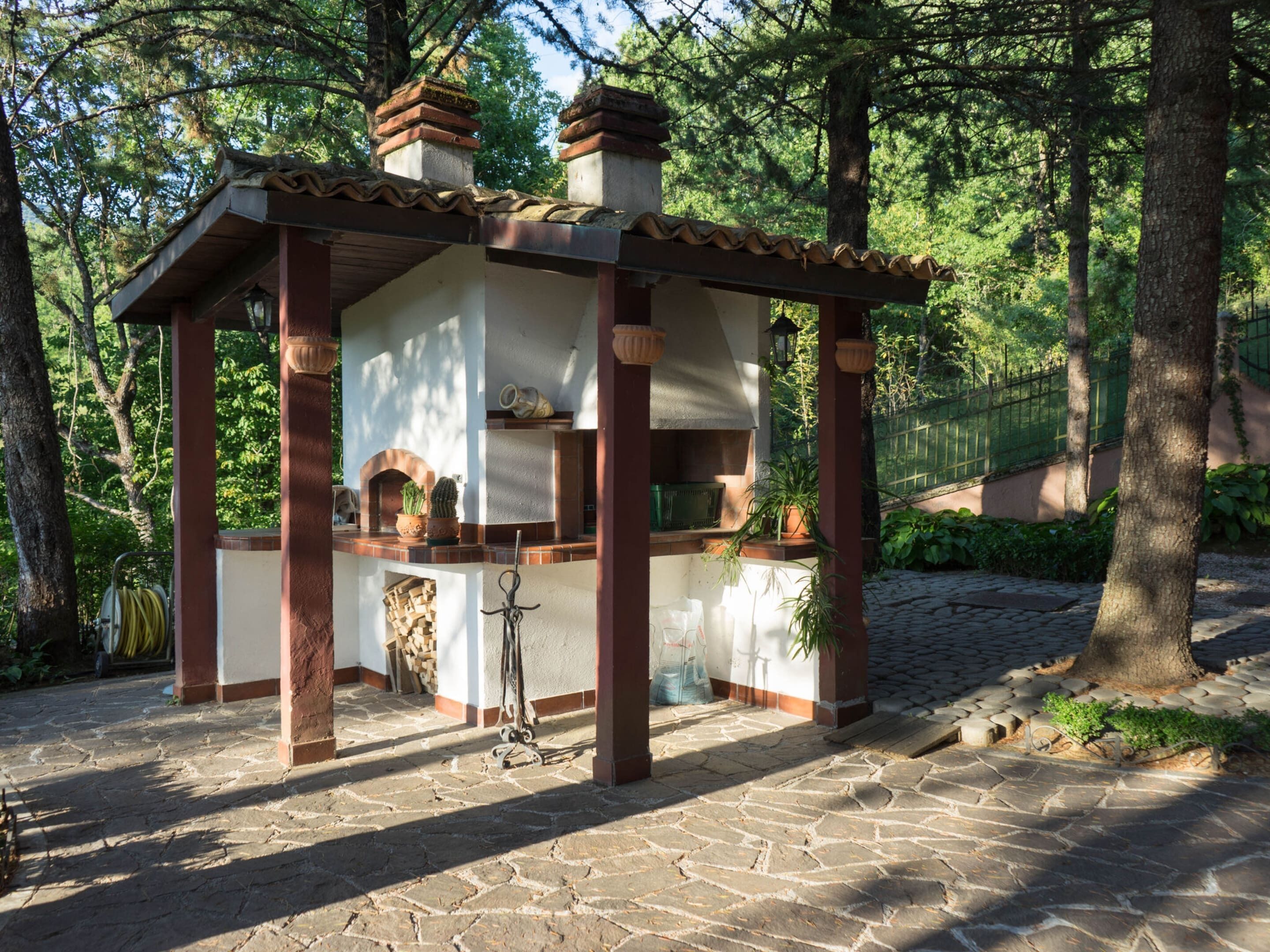 A stone-built outdoor kitchen with a tiled roof, surrounded by trees.