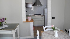 Cuina amb parets de maó blanc, fogó de gas i campana extractora d'acer inoxidable. Hi ha un taulell de fusta amb estovell floral i gerra blanca amb flors.