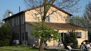Una casa de dues plantes amb teulada de rajola, un jardí amb flors blanques i mobiliari exterior.