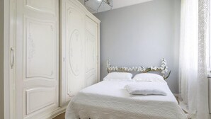 Un dormitori amb un armari gran de color blanc, un llit amb roba de llit blanca i un panell de capçal de fusta.