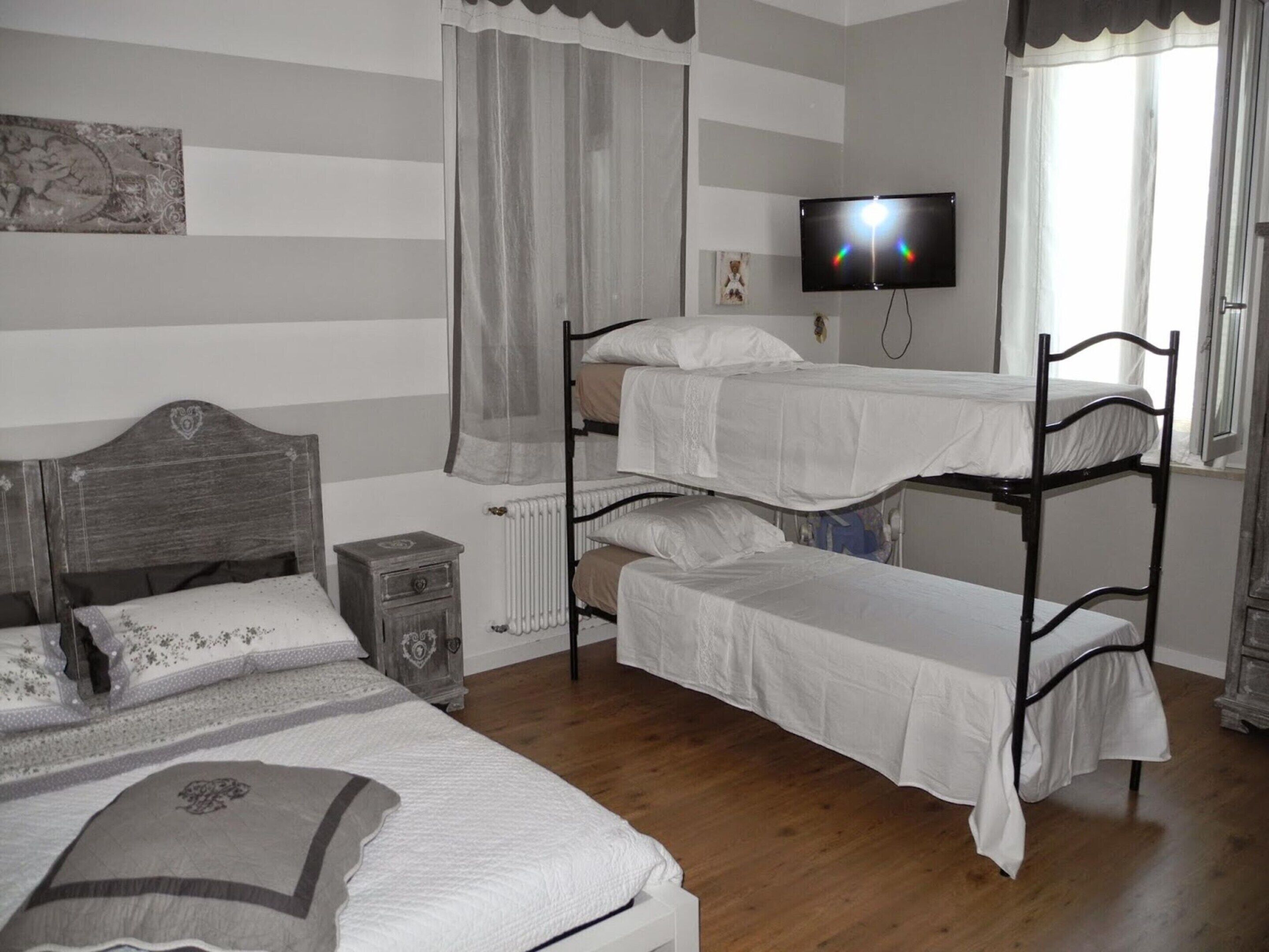 A dormitory room with bunk beds, a bedside table, a radiator, and a television on the wall.
