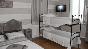 A dormitory room with bunk beds, a bedside table, a radiator, and a television on the wall.