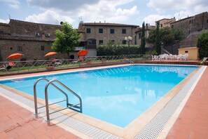 A swimming pool with a metal ladder, surrounded by a tiled deck, with outdoor seating and stone buildings in the background. - Holiday Home in Chianti With Pool & Garden (Barberino Tavarnelle)