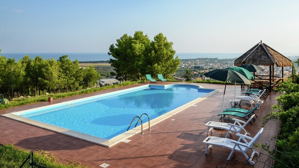 A rectangular swimming pool with a wooden deck, surrounded by lounge chairs and a thatched-roof structure. - Holiday Home in Cropani Marina With Pool (Badolato)
