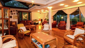 A spacious living room with wooden furniture, a coffee table with books, and a large window overlooking greenery. - Holiday Home in Cropani Marina With Pool (Badolato)